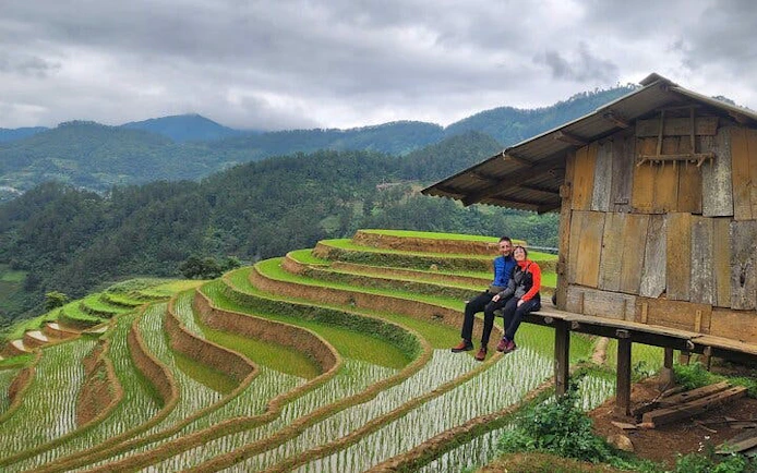 Terraced rice fields in Mu Cang Chai with travelers sitting by a wooden hut.