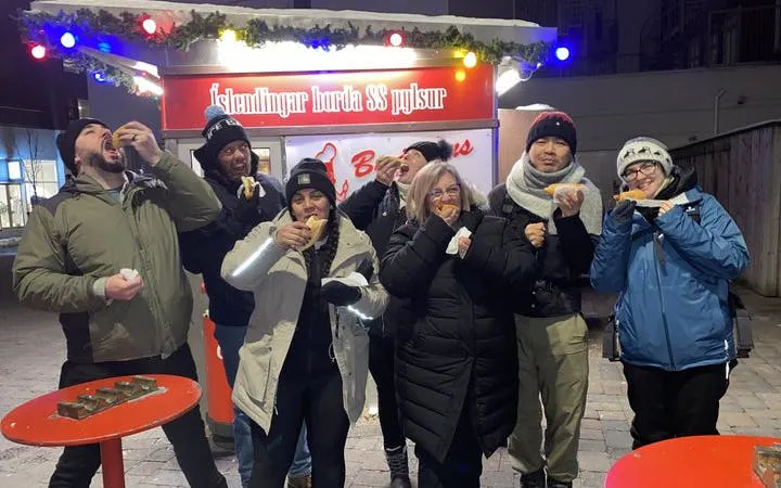 Tourists enjoying hot dogs at an Icelandic food stand during a guided history tour.