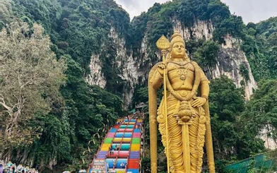 Golden Lord Murugan statue at Batu Caves entrance with colorful steps, Kuala Lumpur.