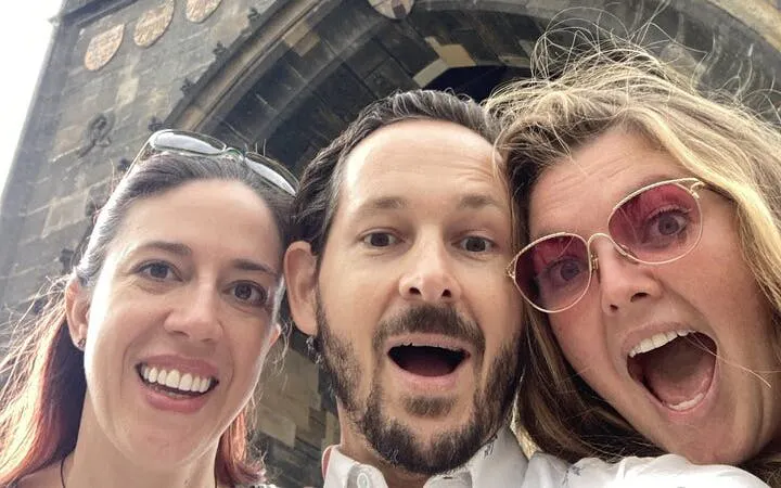 Tourists excitedly pose in front of a Gothic archway in Prague during a self-guided city exploration game.
