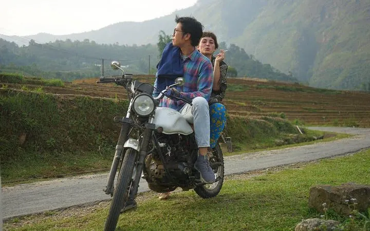 Motorbike riders on a rural road in Sapa with terraced fields and mountains in the background.