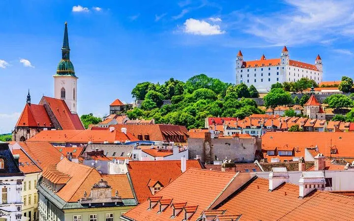 Bratislava Castle and St. Martin's Cathedral viewed from city rooftops on a sunny day.
