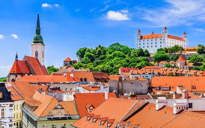 Bratislava Castle and St. Martin's Cathedral viewed from city rooftops on a sunny day.