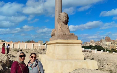 Sphinx statue at Alexandria Port with cityscape in the background.