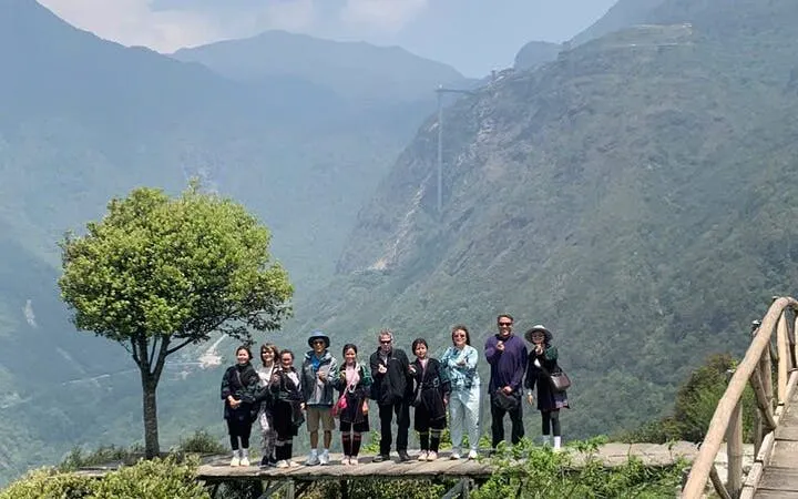 Group of tourists at Lonely Tree viewpoint, Sapa, with mountains and Glass Bridge in the background.