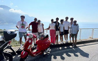 Group on Vespa tour overlooking Amalfi Coast with sea view and mountains in background.