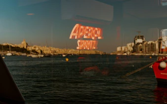 Aperol Spritz sign reflecting on water during sunset cruise in Malta.