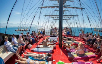 Pirate-themed boat with tourists sunbathing on deck, Alanya coast in background.