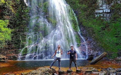 Visitors at Love Waterfall in Sapa, Vietnam, standing on rocks with cascading water in the background.