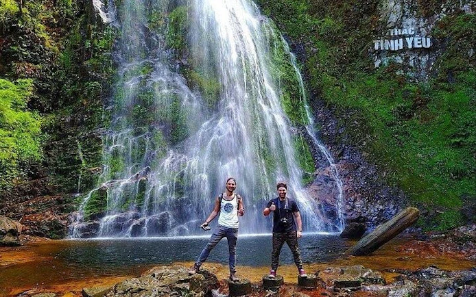 Visitors at Love Waterfall in Sapa, Vietnam, standing on rocks with cascading water in the background.
