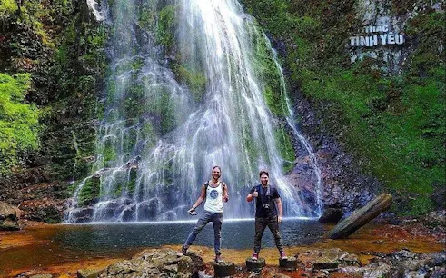 Visitors at Love Waterfall in Sapa, Vietnam, standing on rocks with cascading water in the background.