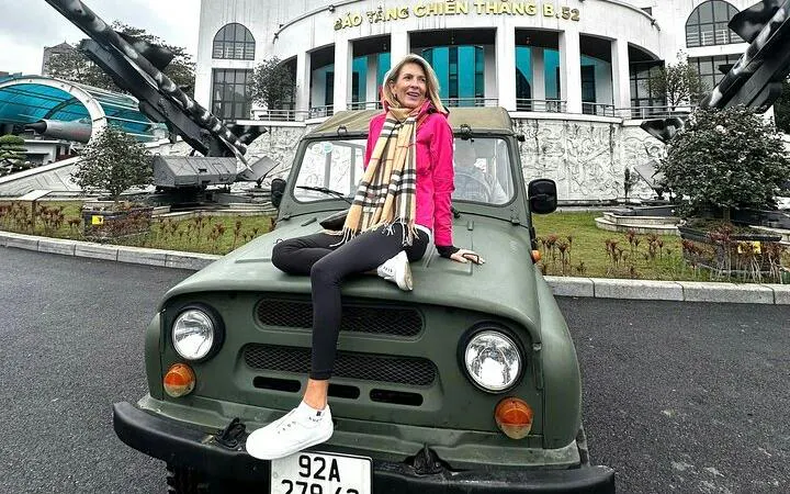 Hanoi Jeep tour participant sitting on vintage jeep in front of B-52 Victory Museum, Hanoi.