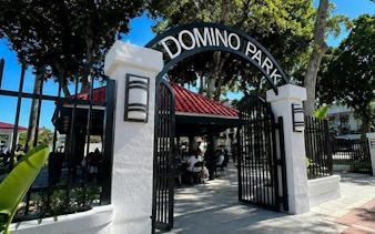 Domino Park entrance on Calle Ocho, Miami, with visitors enjoying the shaded area.