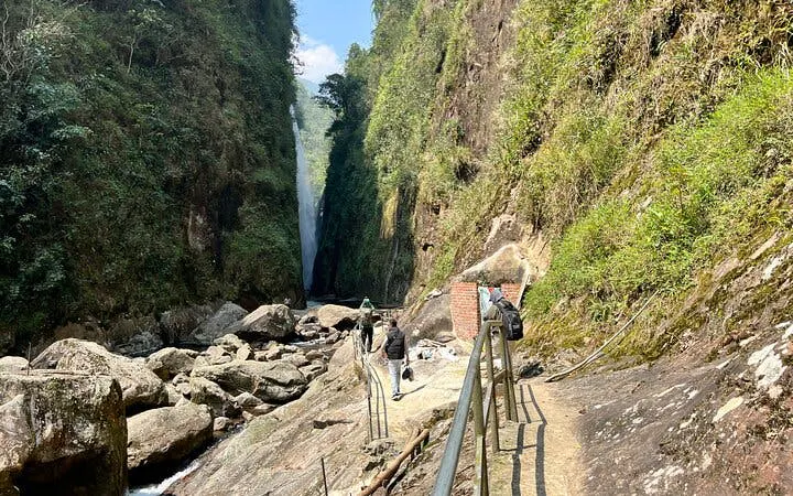 Motorbike tour group walking towards Dragon Waterfall in Sapa, Vietnam, along a rocky path.