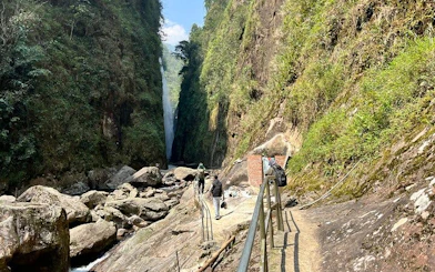 Motorbike tour group walking towards Dragon Waterfall in Sapa, Vietnam, along a rocky path.