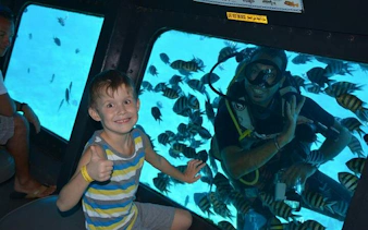 Child inside semi-submarine viewing diver and fish in Hurghada sea trip.