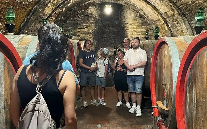 Tour group exploring a wine cellar in Montepulciano, Italy, with large wooden barrels.