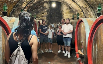 Tour group exploring a wine cellar in Montepulciano, Italy, with large wooden barrels.