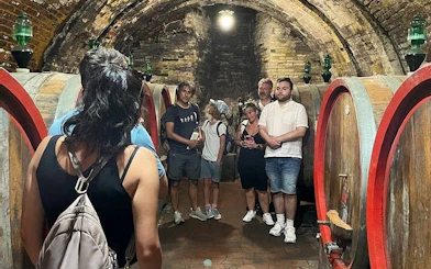Tour group exploring a wine cellar in Montepulciano, Italy, with large wooden barrels.