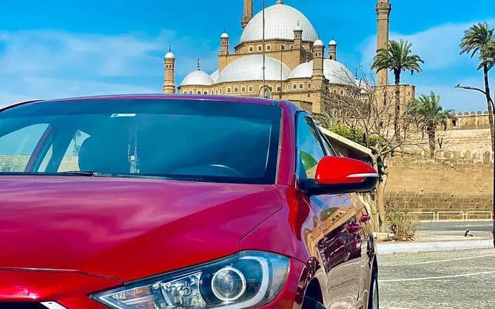 Red car in front of the Citadel of Saladin, Cairo, with mosque domes in the background.
