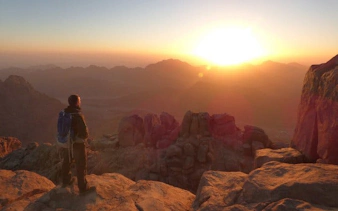 Hiker watching sunrise from Moses Mountain summit near Saint Catherine Monastery, Sinai.