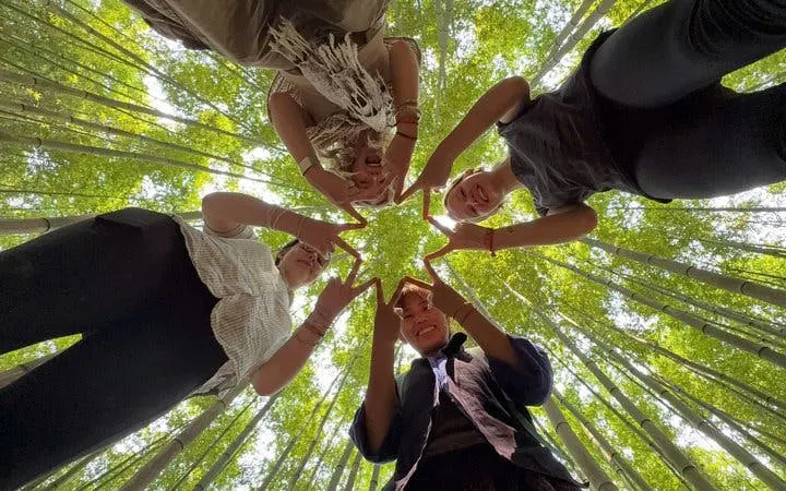 Group forming star shape with fingers under bamboo canopy, Mu Cang Chai motorbike tour.