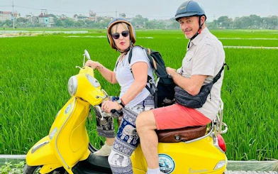 Couple riding a yellow Vespa through rice fields on Hanoi Countryside Half-day Vespa Tour.