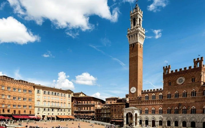 Siena's Piazza del Campo with Torre del Mangia under a blue sky.