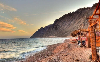 Coastal view of Dahab with mountains and beach huts, part of 3 Pools Dahab Trip from Sharm El Sheikh.
