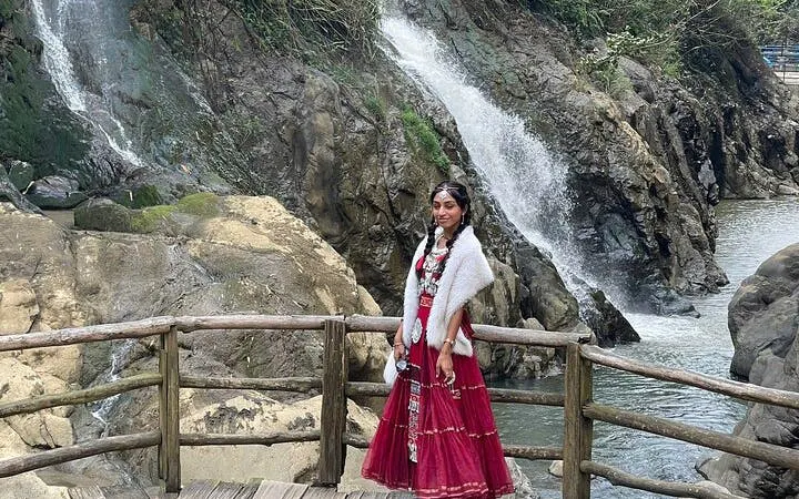 Woman in traditional attire on a wooden bridge near a waterfall in Cat Cat Village, Sa Pa.