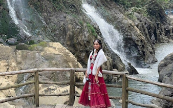 Woman in traditional attire on a wooden bridge near a waterfall in Cat Cat Village, Sa Pa.