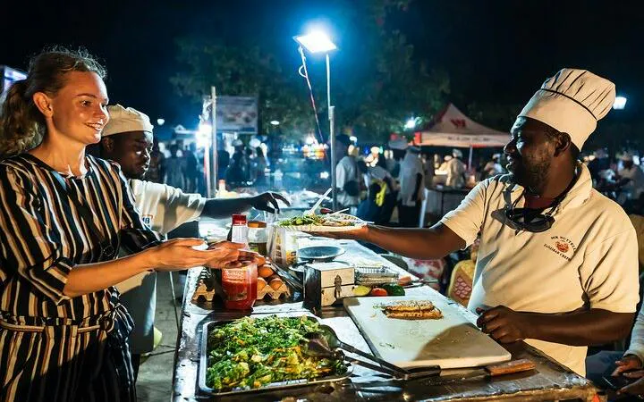 Vendor serving food at Stone Town Night Market, Zanzibar, with tourists exploring local cuisine.