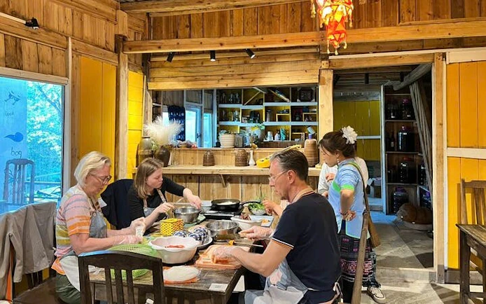Cooking class participants preparing Bun Cha in a Vietnamese family kitchen setting.