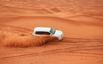 SUV driving through desert dunes during morning safari in Dubai.