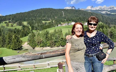 Two people smiling with Dolomites mountains and lush greenery in the background, Verona tour.