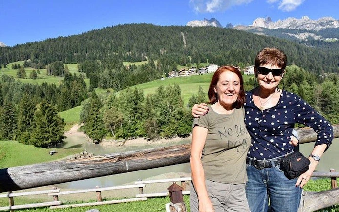 Two people smiling with Dolomites mountains and lush greenery in the background, Verona tour.
