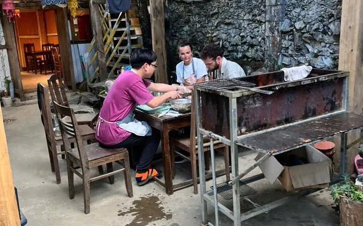 Bun Cha cooking class participants preparing Vietnamese dish in a rustic family-style setting.