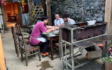 Bun Cha cooking class participants preparing Vietnamese dish in a rustic family-style setting.