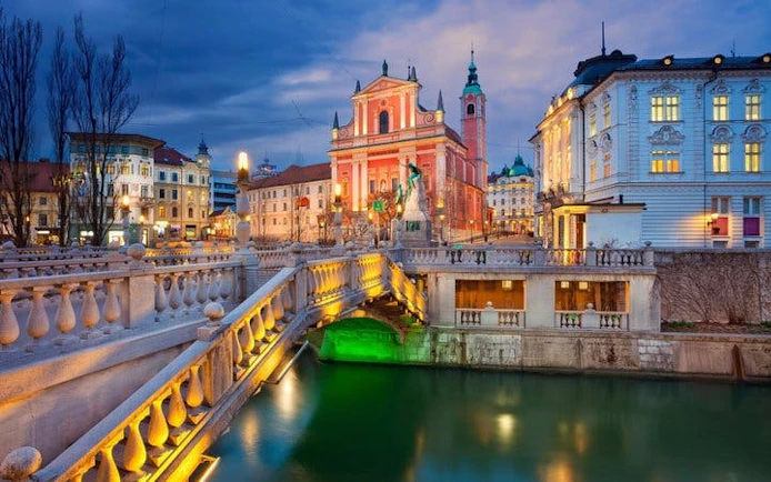 Franciscan Church and Triple Bridge in Ljubljana at dusk on self-guided walking tour.