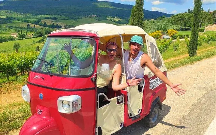 Tuk Tuk on Tuscany wine tour with guide, vineyards in background.