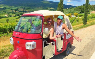 Tuk Tuk on Tuscany wine tour with guide, vineyards in background.