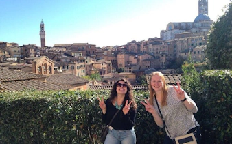 Two tourists in Siena with cityscape and Torre del Mangia in the background.