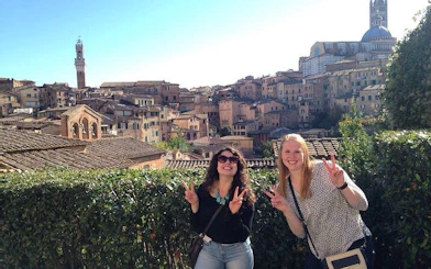 Two tourists in Siena with cityscape and Torre del Mangia in the background.