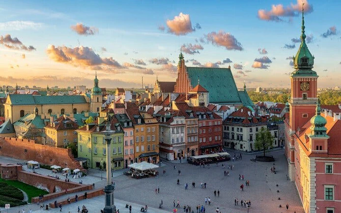 Warsaw Old Town Square with colorful buildings and Royal Castle tower.