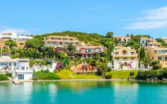 Colorful coastal houses in Menorca viewed from the water, part of a self-guided walking tour.