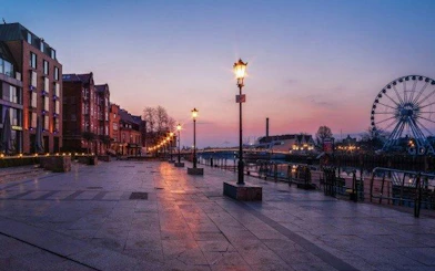 Gdansk waterfront promenade at sunset with Ferris wheel and historic buildings.