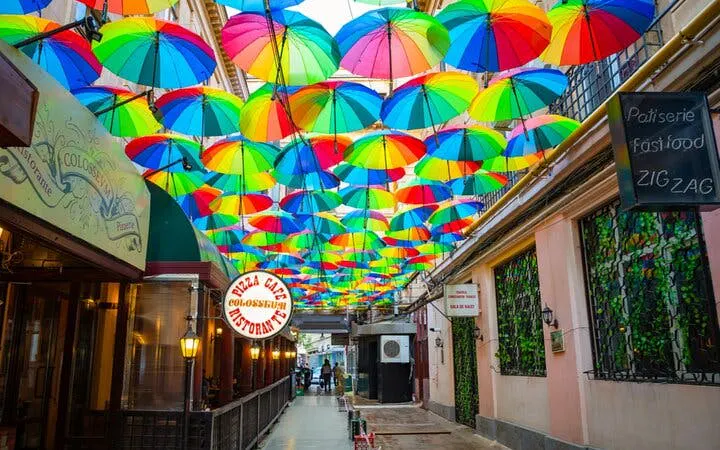Colorful umbrellas hanging over a narrow street in Old Town Bucharest, part of a self-guided city exploration game.