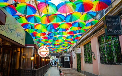 Colorful umbrellas hanging over a narrow street in Old Town Bucharest, part of a self-guided city exploration game.