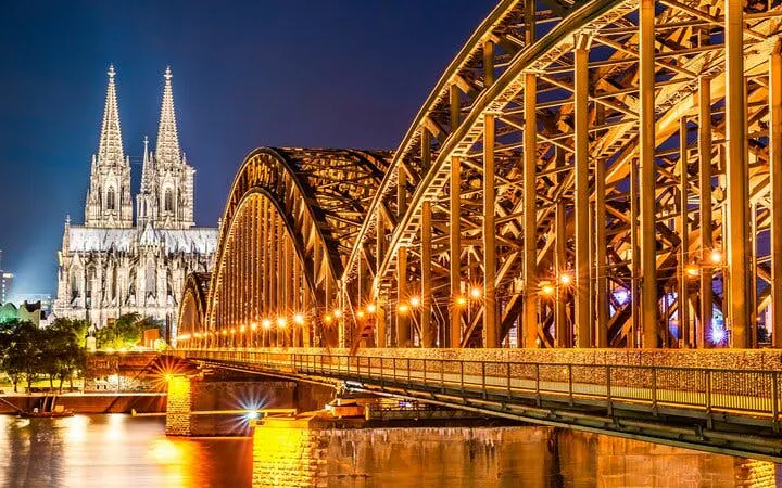 Cologne Cathedral and Hohenzollern Bridge illuminated at night, part of haunted city exploration game.