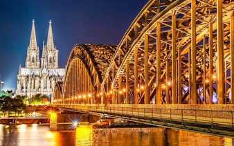 Cologne Cathedral and Hohenzollern Bridge illuminated at night, part of haunted city exploration game.